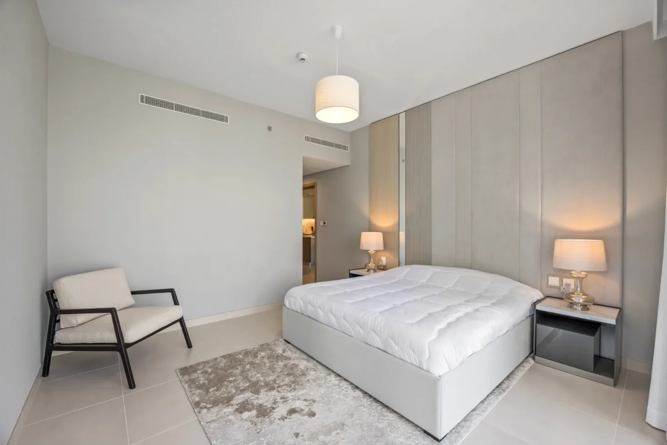 Modern hotel bedroom with a large bed, gray headboard, and soft lamps on each side