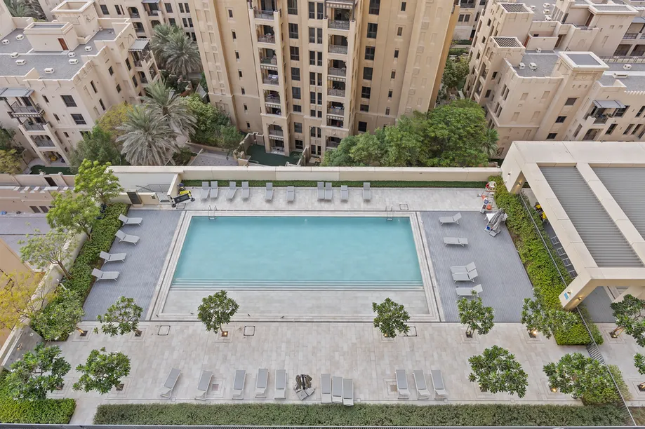Rooftop swimming pool surrounded by lounge chairs and trees in a beige high-rise residential complex.