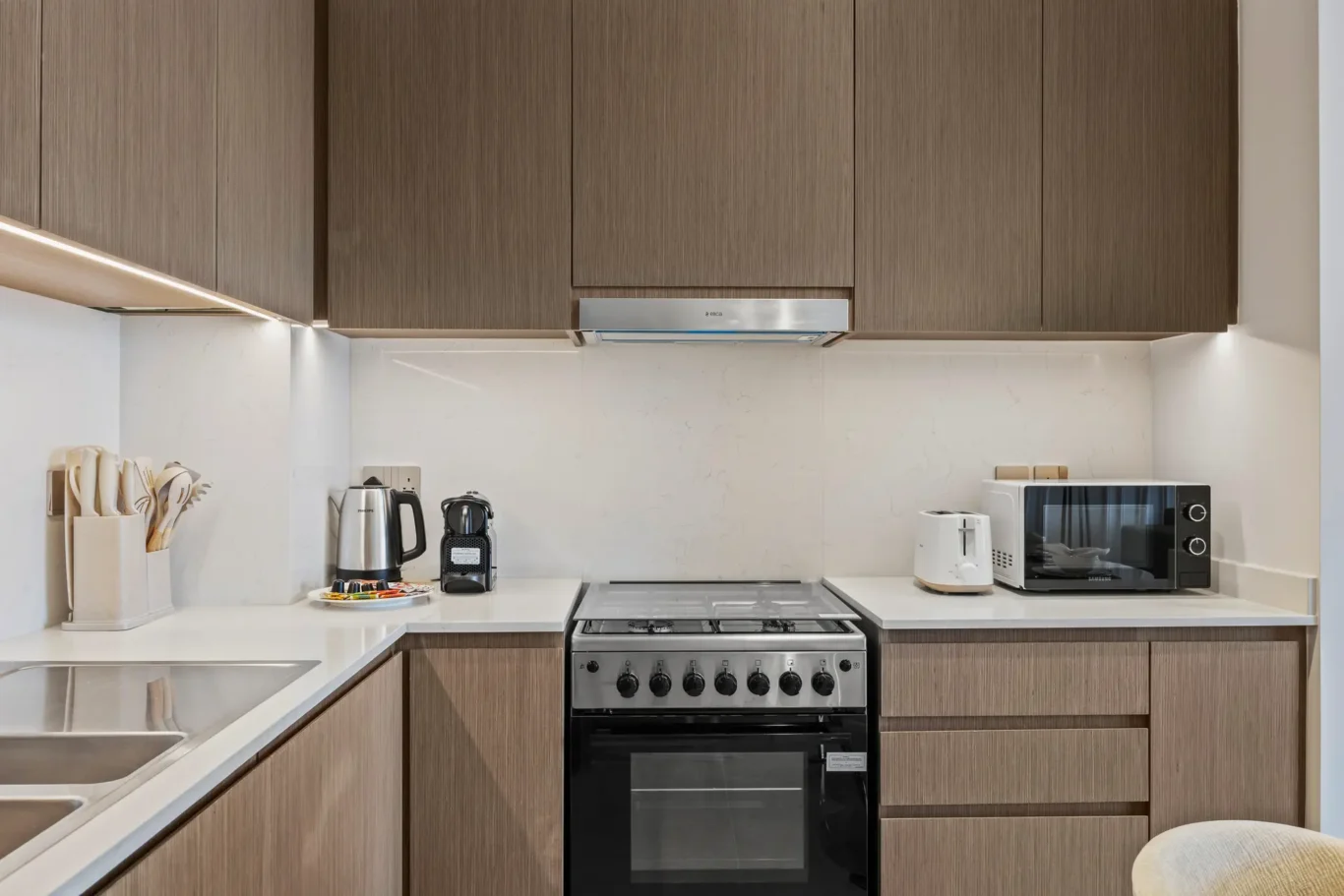 Modern kitchen with brown wood cabinets, stainless steel stove and range hood, and white countertops.