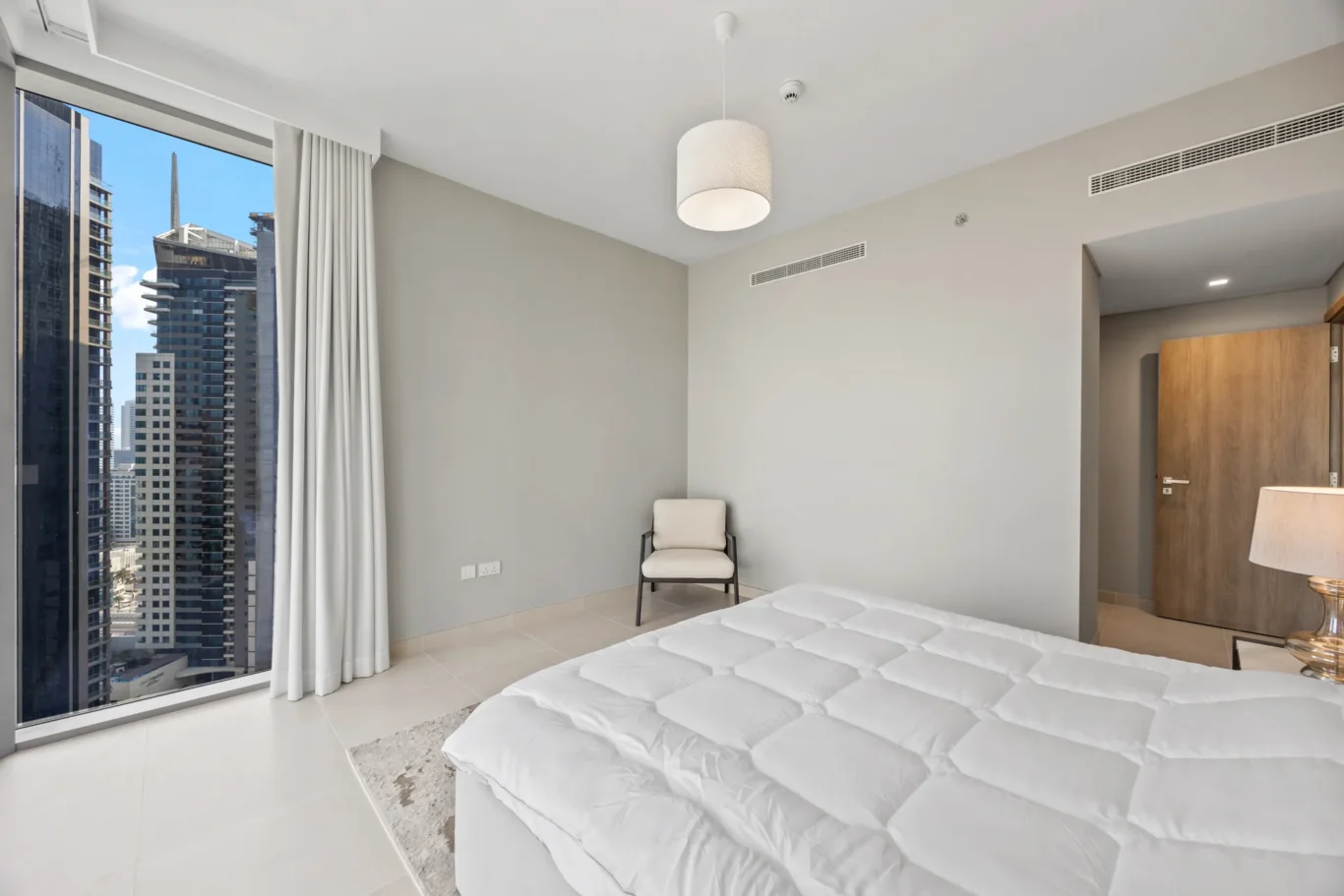 Hotel room with a city skyline view, two white beds, neutral gray walls, and a chair near the corner window.