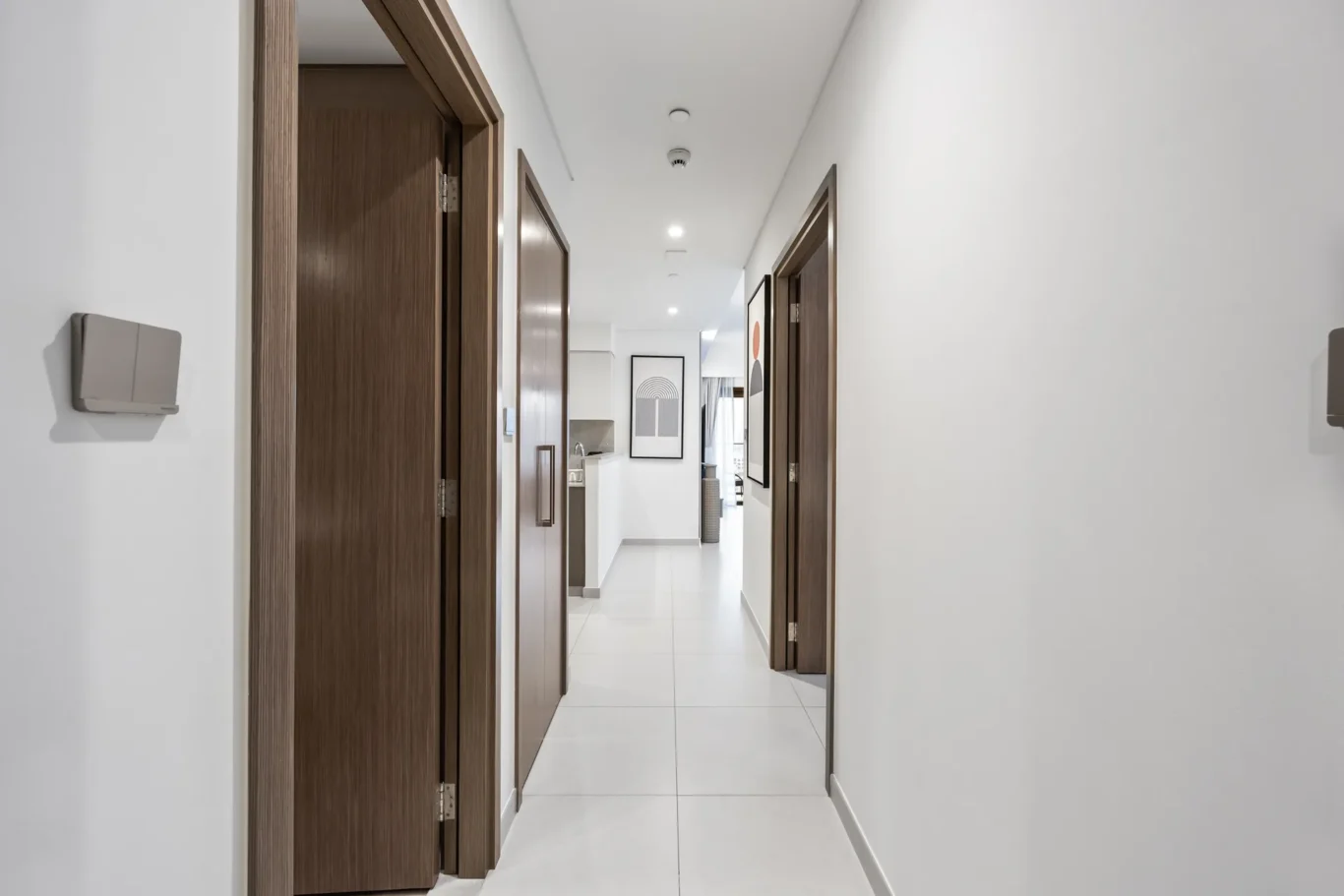 Bright hallway in a modern apartment with white walls, brown wooden doors, and a framed artwork at the far end.