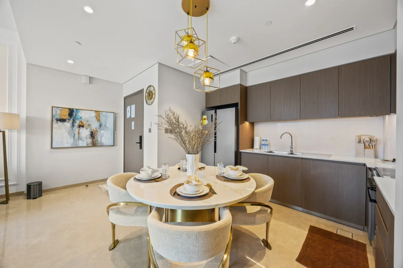 Modern kitchen with dark wood cabinets, marble dining table, and gold pendant lights over a round dining table set for four.