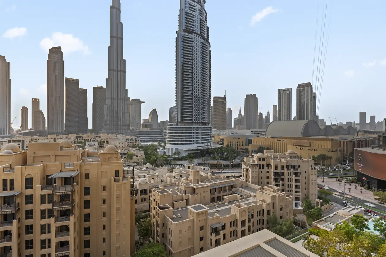 Dubai skyline with the Burj Khalifa towering over beige residential buildings and the Dubai Mall in the background.