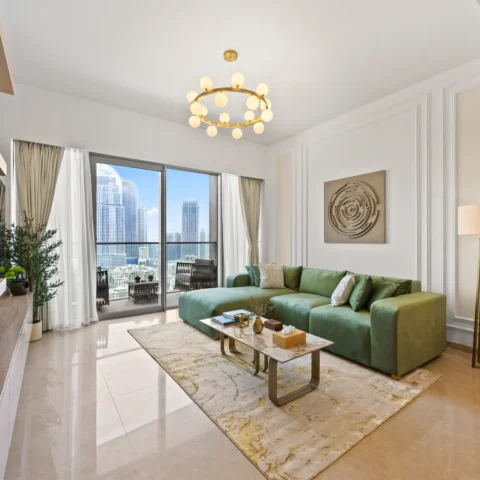 Bright living room with a green sectional sofa, marble coffee table, and a cityscape view through glass doors.