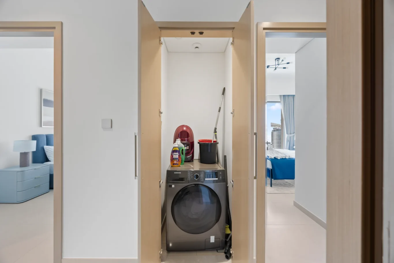 Open closet laundry alcove with a front-loading washing machine, detergent bottles, and a mop bucket inside.