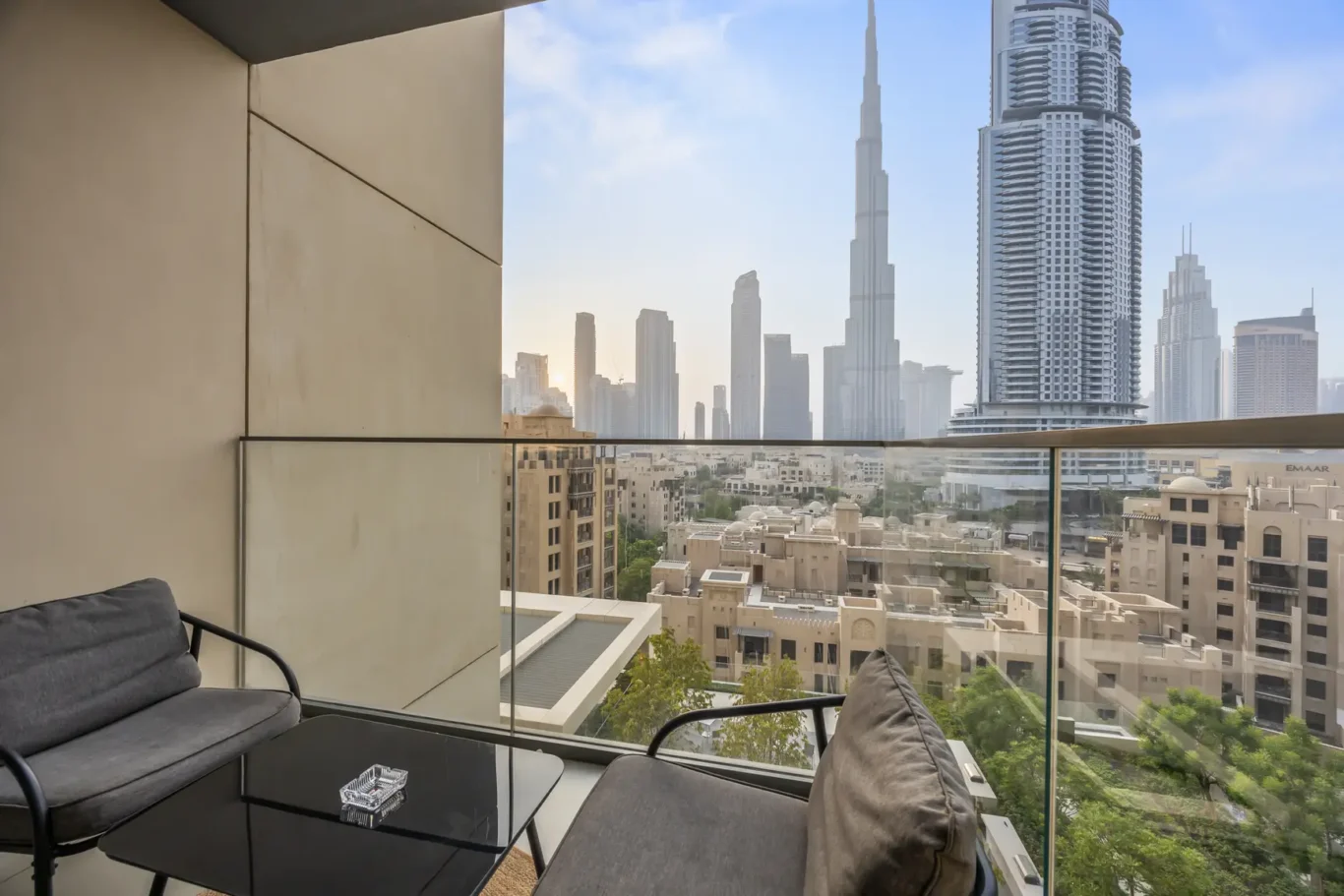 Balcony seating area with dark cushions and a glass coffee table, overlooking a dense city skyline of tall skyscrapers.