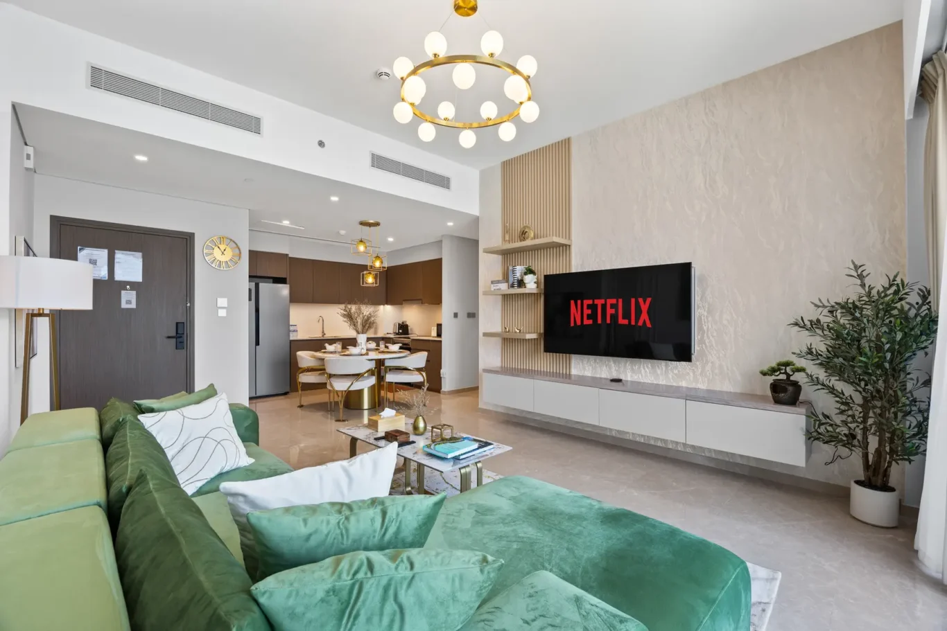 Modern living room with a wall-mounted Netflix screen, a green sectional sofa, and a marble coffee table.