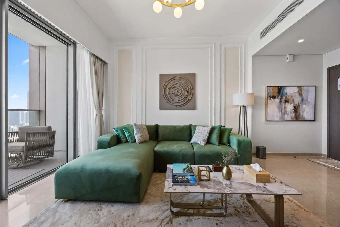 Bright living room with a green sectional sofa, marble coffee table, and large windows overlooking a cityscape.
