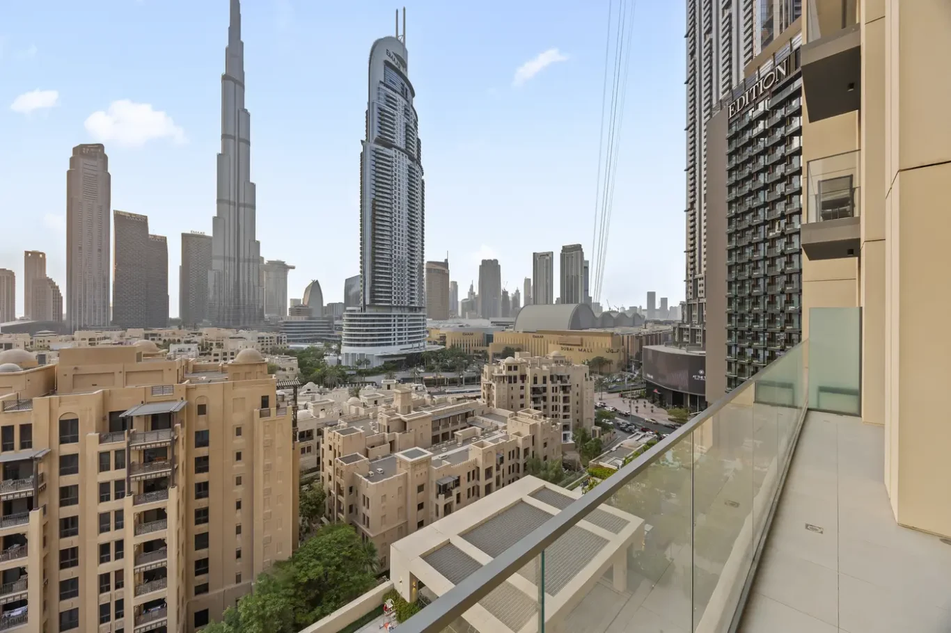 Balcony view overlooking a dense cityscape with beige low-rise buildings in the foreground and tall glass skyscrapers in the distance, including a prominent curved tower.