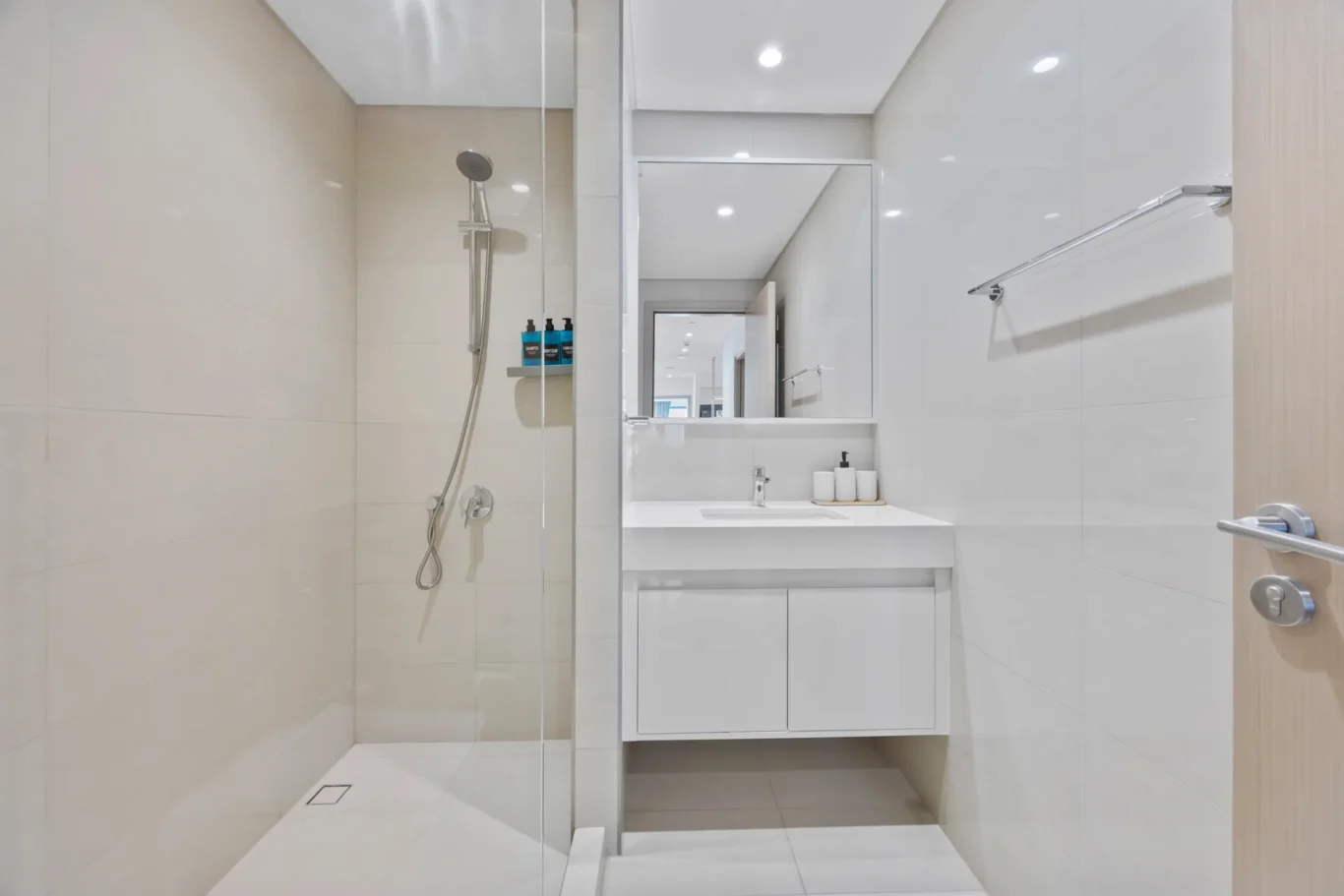 Modern white bathroom with glass shower boundary, wall-to-wall tiles, and a floating vanity with mirror cabinet.