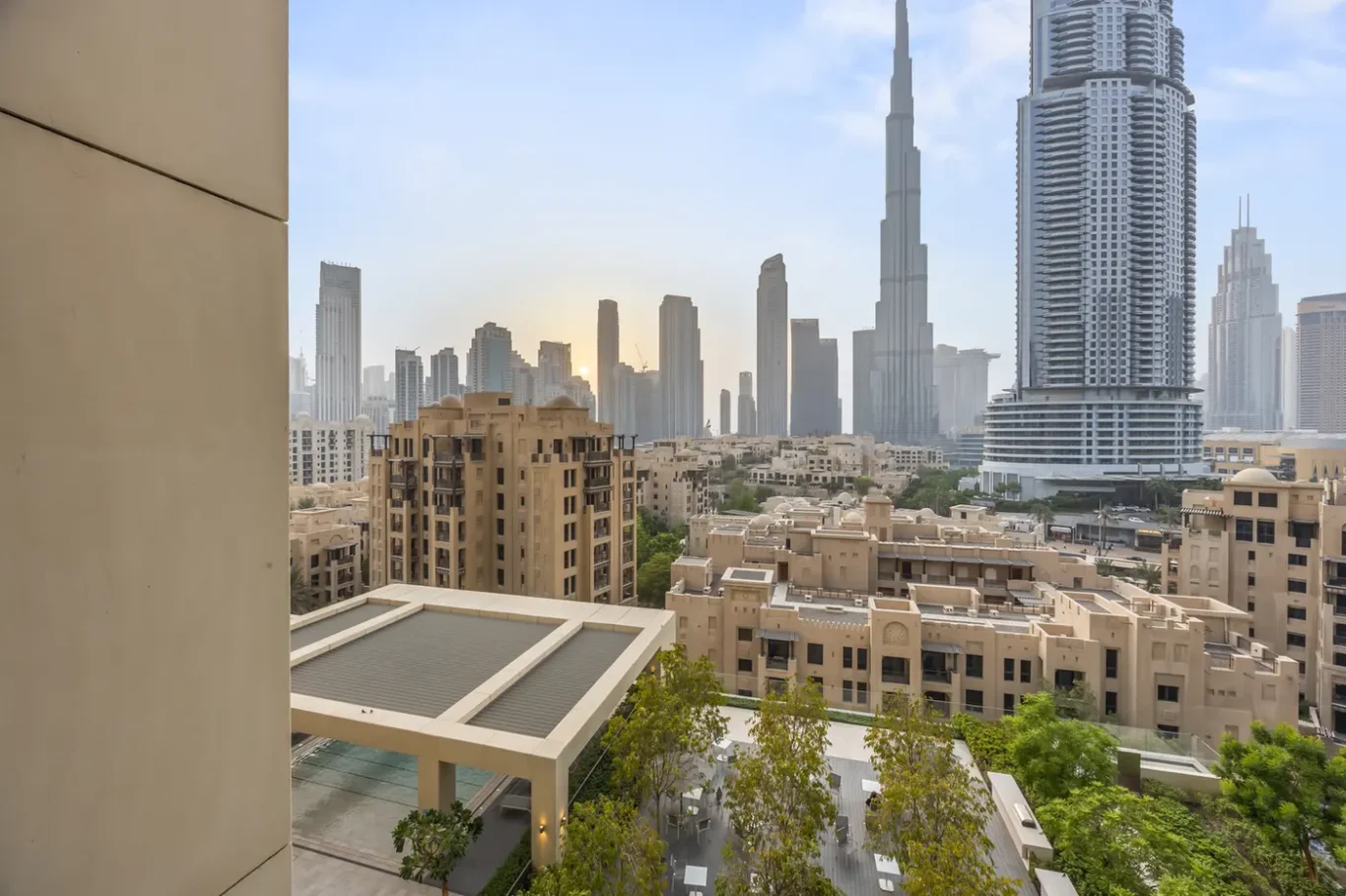 Dubai skyline with beige residential buildings in the foreground and a cluster of modern high-rises in the distance, including the tall Burj Khalifa-like tower far right.