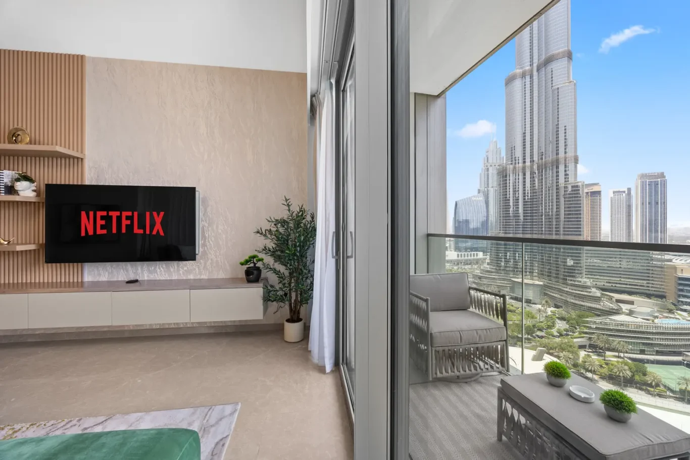 Modern living room with a wall-mounted TV showing Netflix, beige textured wall and a plant by the cabinet.