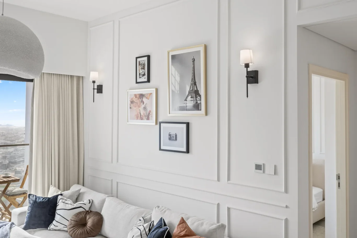 Living room gallery wall with four framed prints on a light gray paneled wall and two wall sconces beside them.