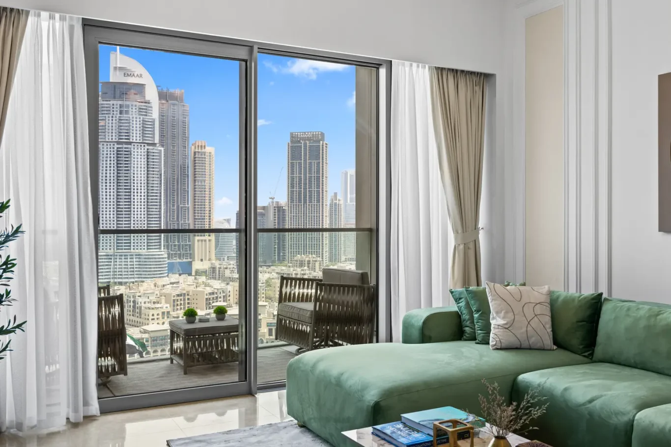 Living room with a green sectional sofa and large glass doors opening to a balcony with a city skyline outside.