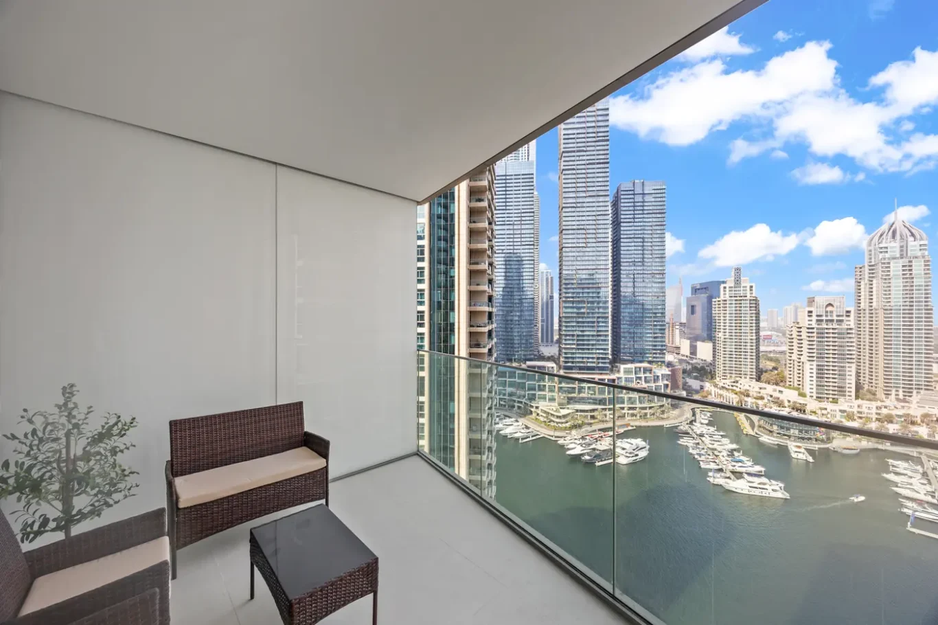 Balcony with wicker seating overlooking a marina and city skyscrapers on a sunny day