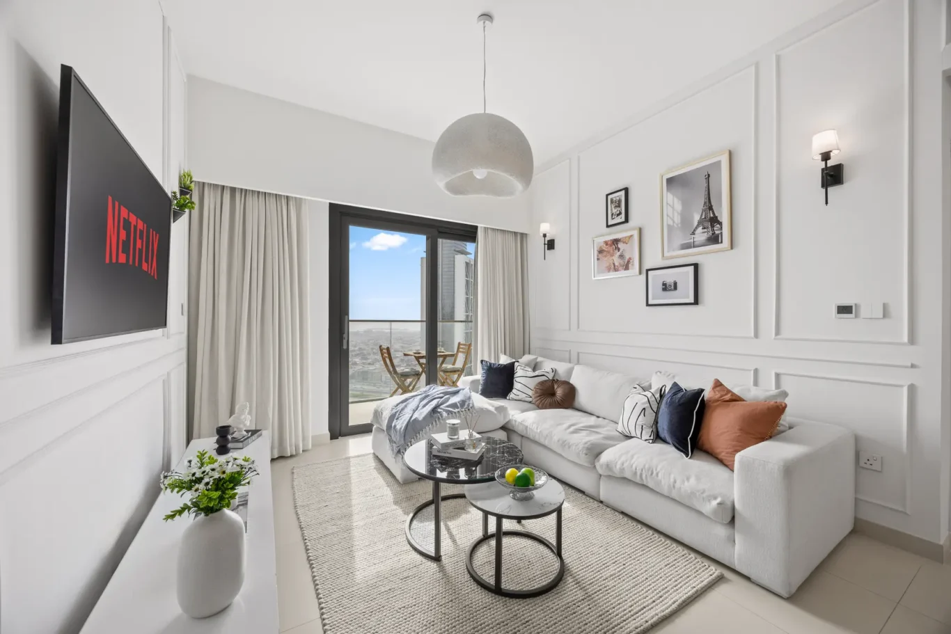 Bright living room with white walls, a large wall-mounted TV, and a gray sectional sofa facing a balcony view.