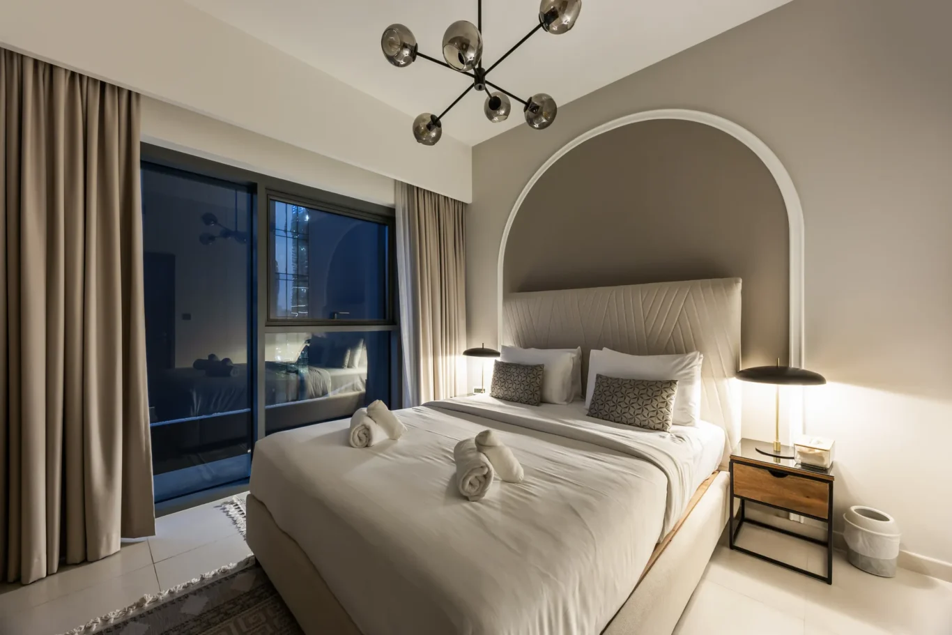 Hotel room with two neatly made beds, a curved arched headboard niche, and warm bedside lamps on each side.