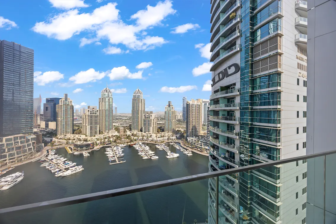 Marina with numerous yachts docked in calm water, surrounded by modern glass high-rise buildings.