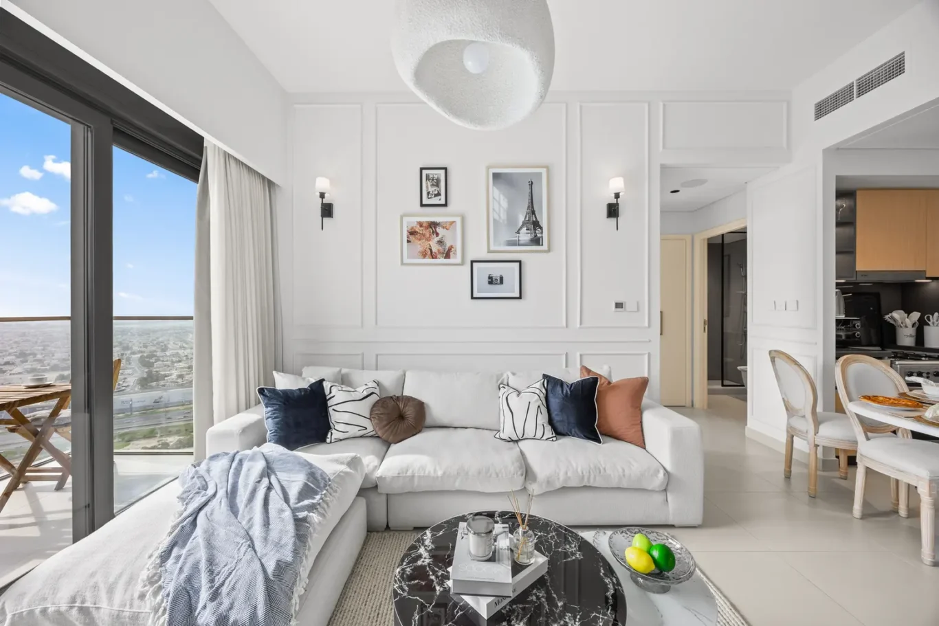 Bright living room with white walls and a gallery wall above a light sofa, navy and rust cushions, and a round marble coffee table.