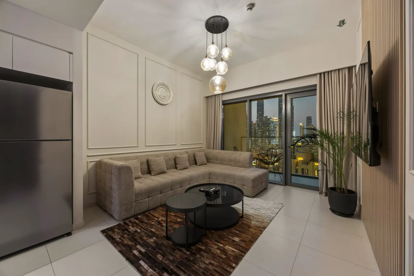 Modern living room with an L-shaped beige sectional, glass coffee tables, and a city view through sliding glass doors.