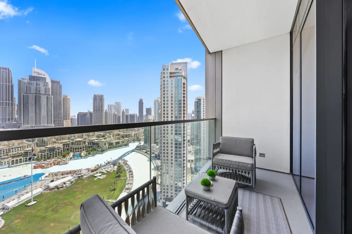 Balcony seating area with gray cushions overlooks a city skyline and pool below on a sunny day.
