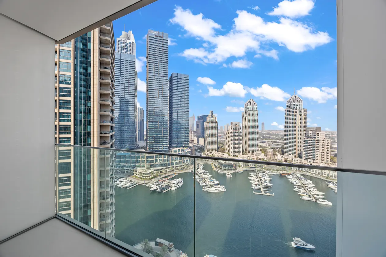 Balcony overlook of a modern city skyline with glass skyscrapers and a marina full of yachts under a blue sky.