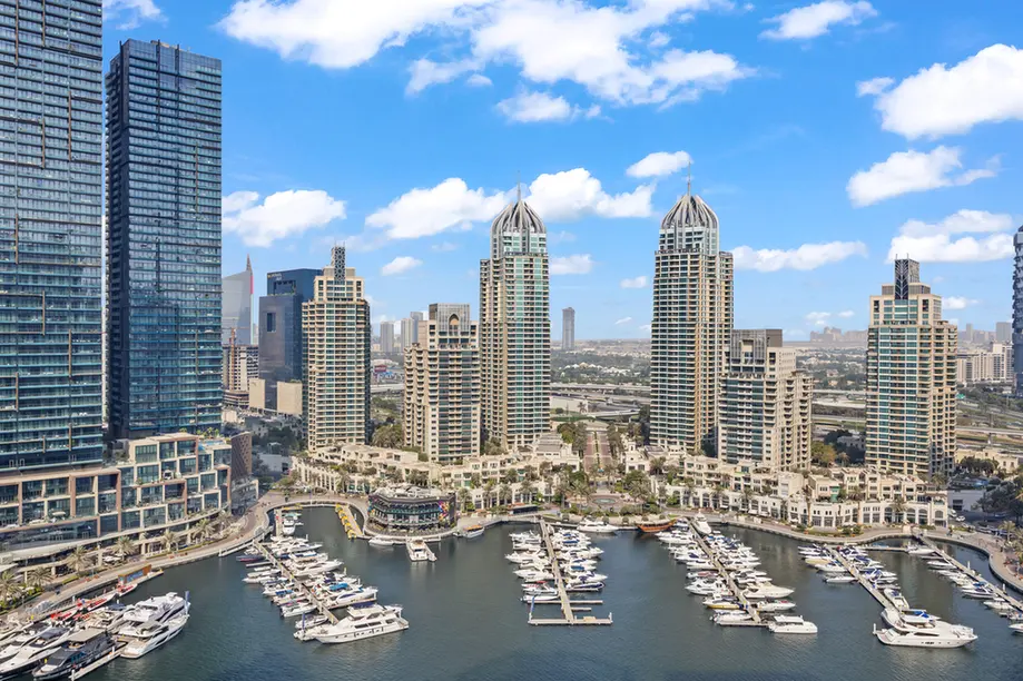 Dubai Marina skyline with tall residential towers and a marina filled with numerous yachts and boats under a blue sky.
