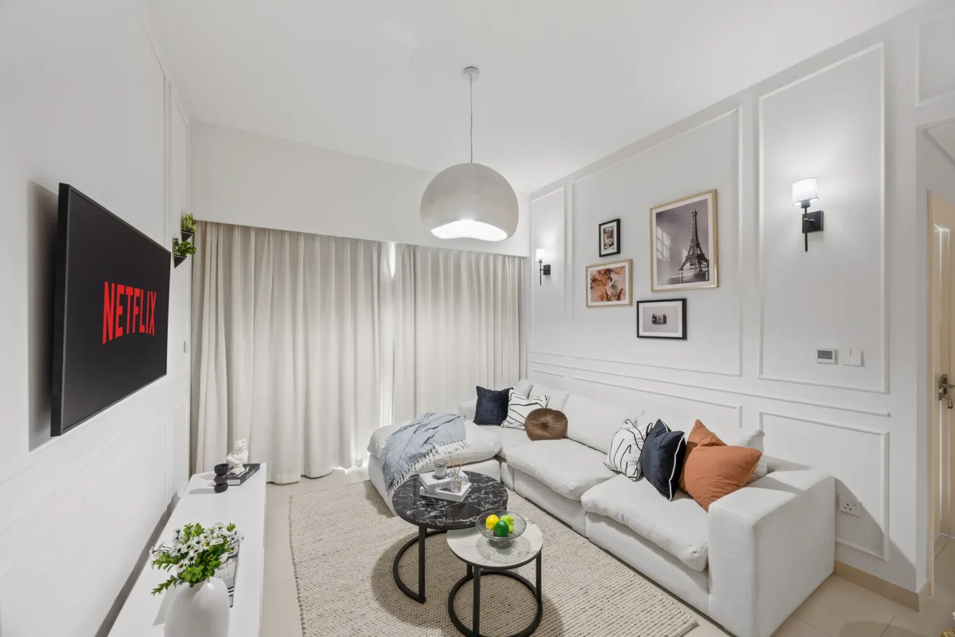 Bright living room with white paneled walls, a light-gray sectional sofa, and two black nesting coffee tables by a beige rug.