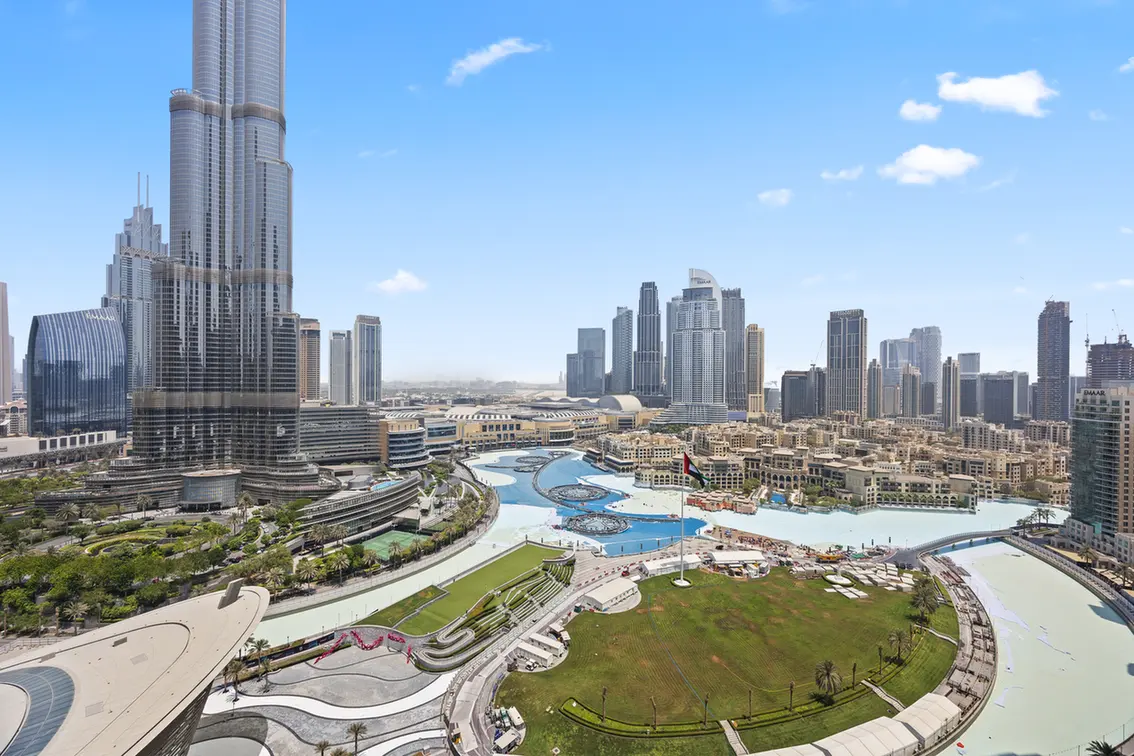 Aerial view of Dubai skyline with Burj Khalifa, tall glass towers, and a winding aqua water-park below near a green lawn.