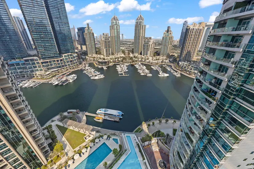 Aerial view of a marina with many yachts, bordered by tall skyscrapers and modern towers.] ,