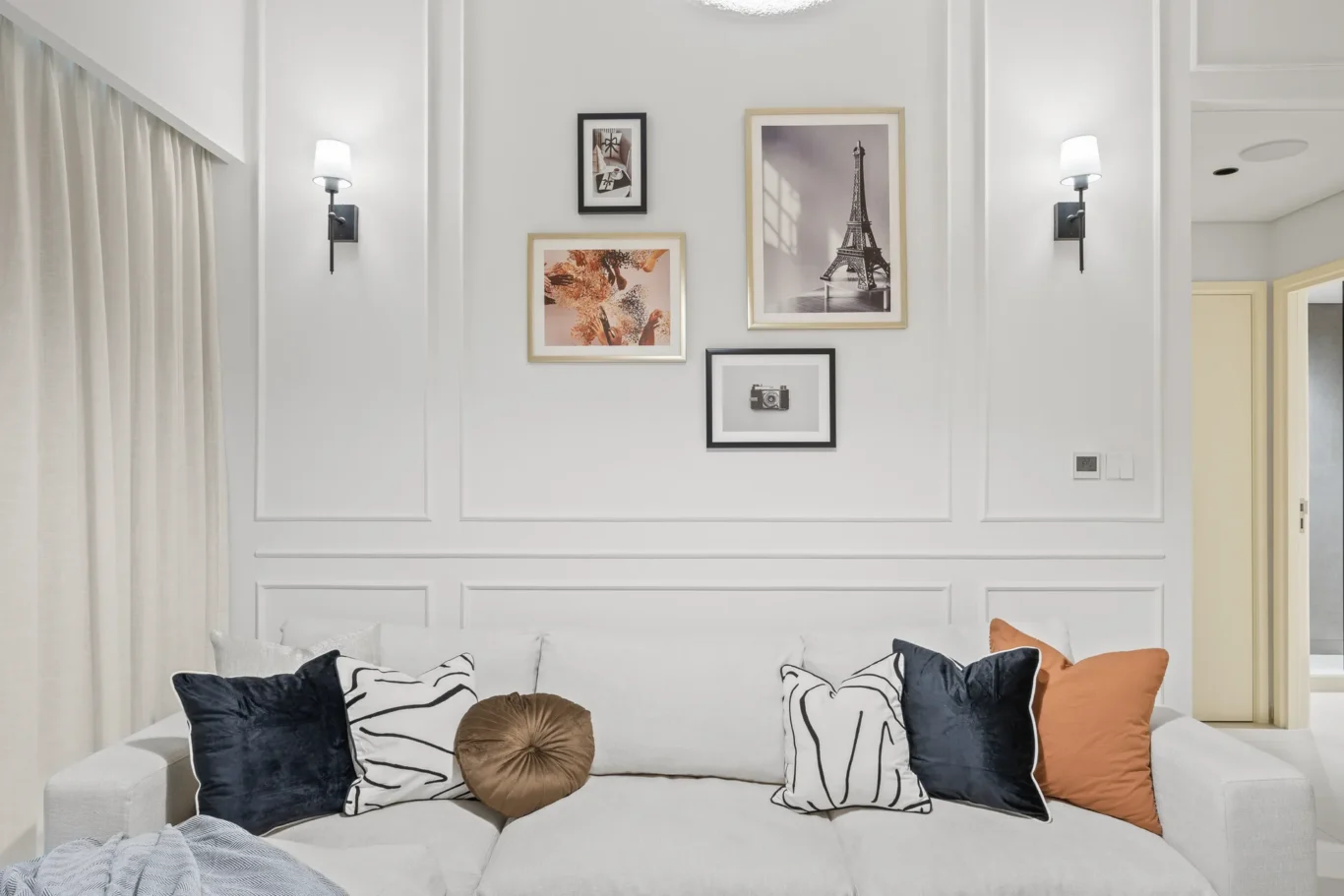 Gallery wall of five frames above a light gray sofa with black, white, and orange cushions in a bright living room.
