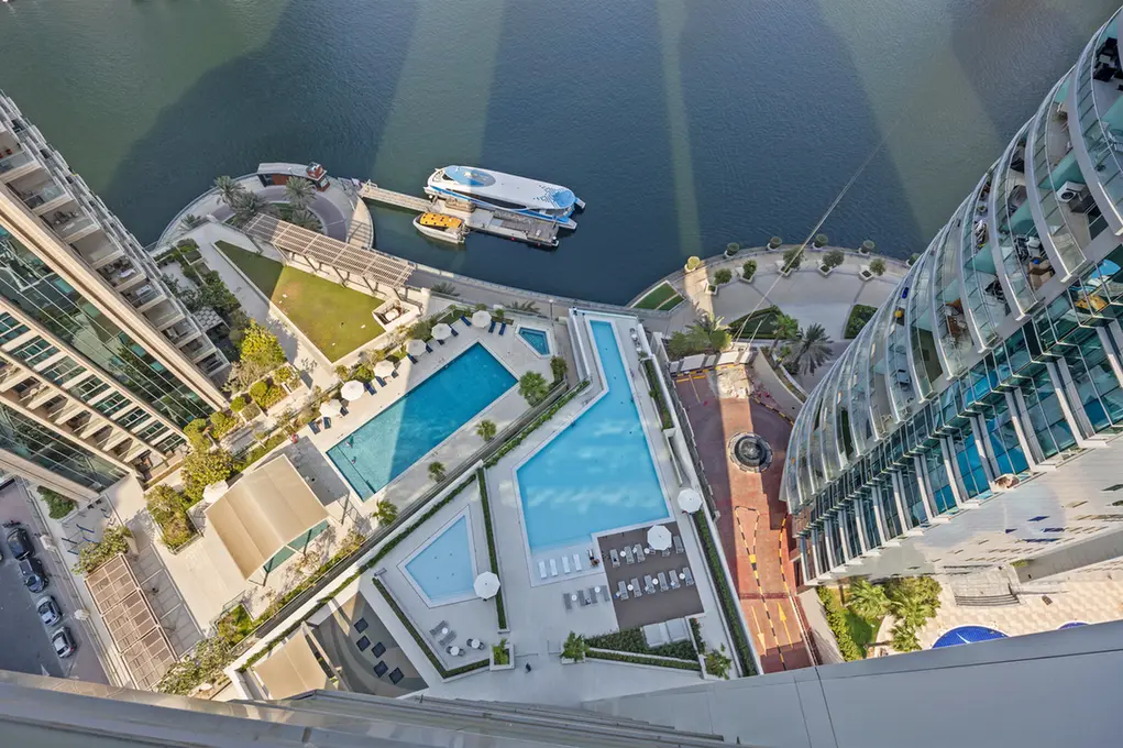 Aerial view of a waterfront condominium complex with multiple pools and a docked boat in a marina area