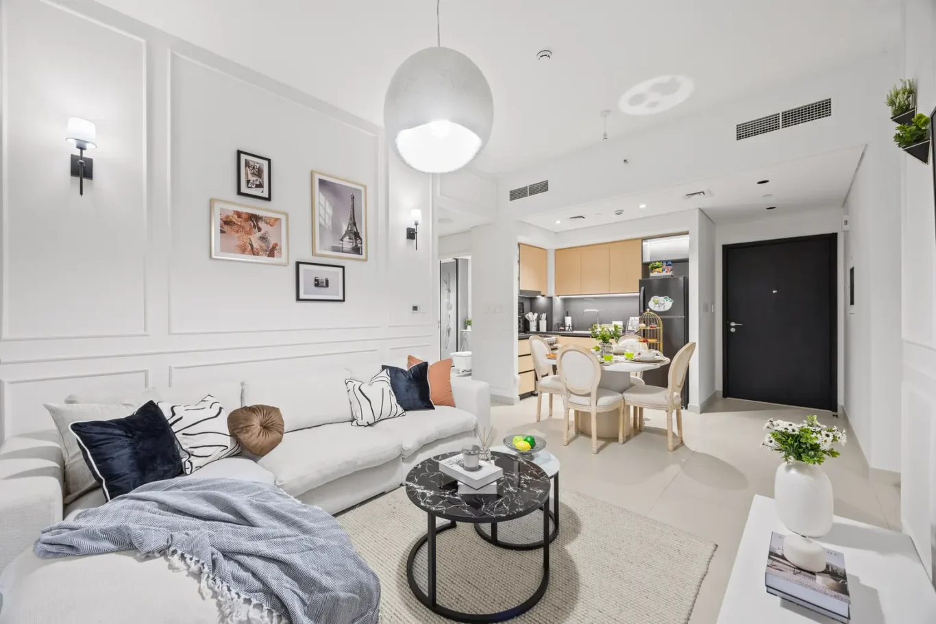 Bright open-plan living room with a gray sofa, colorful cushions, and a round black marble coffee table near the dining area.