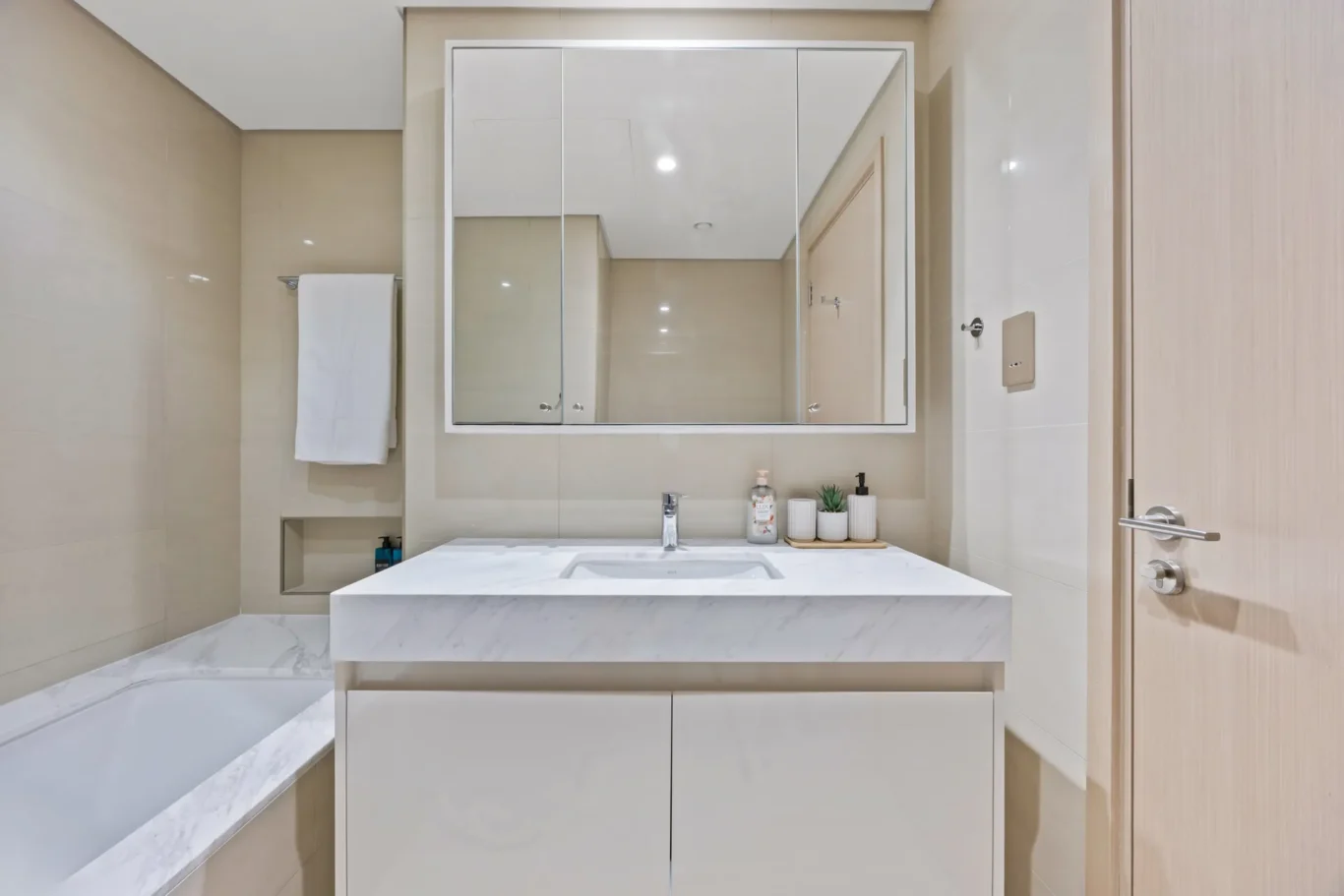 Modern bathroom vanity with white marble countertop, undermount sink, and mirrored cabinet above you can see in the reflection