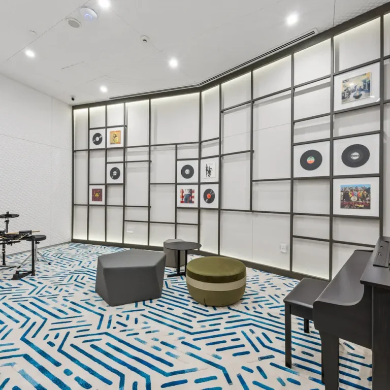 Music rehearsal room with a electronic drum kit on the left, a black piano on the right, and geometric wall panels displaying records and pictures behind.