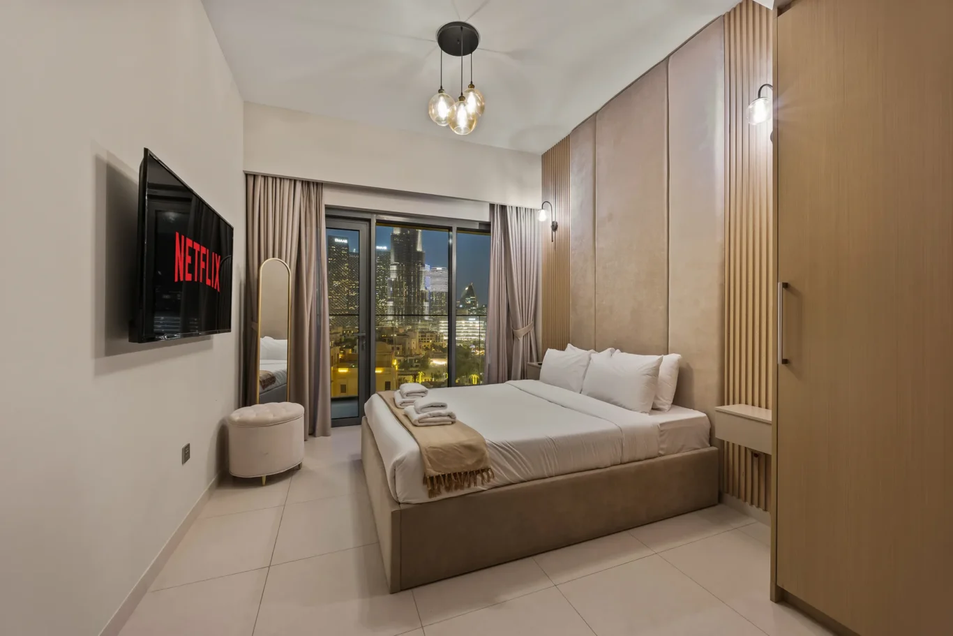 Hotel room with two white beds, beige headboard, and a city skyline view through glass doors at night.