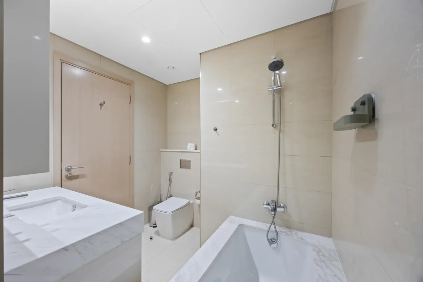 Modern bathroom with a marble countertop sink, beige tiled walls, a wall-mounted handheld shower, and a.toilet nearby for a sleek, contemporary look.