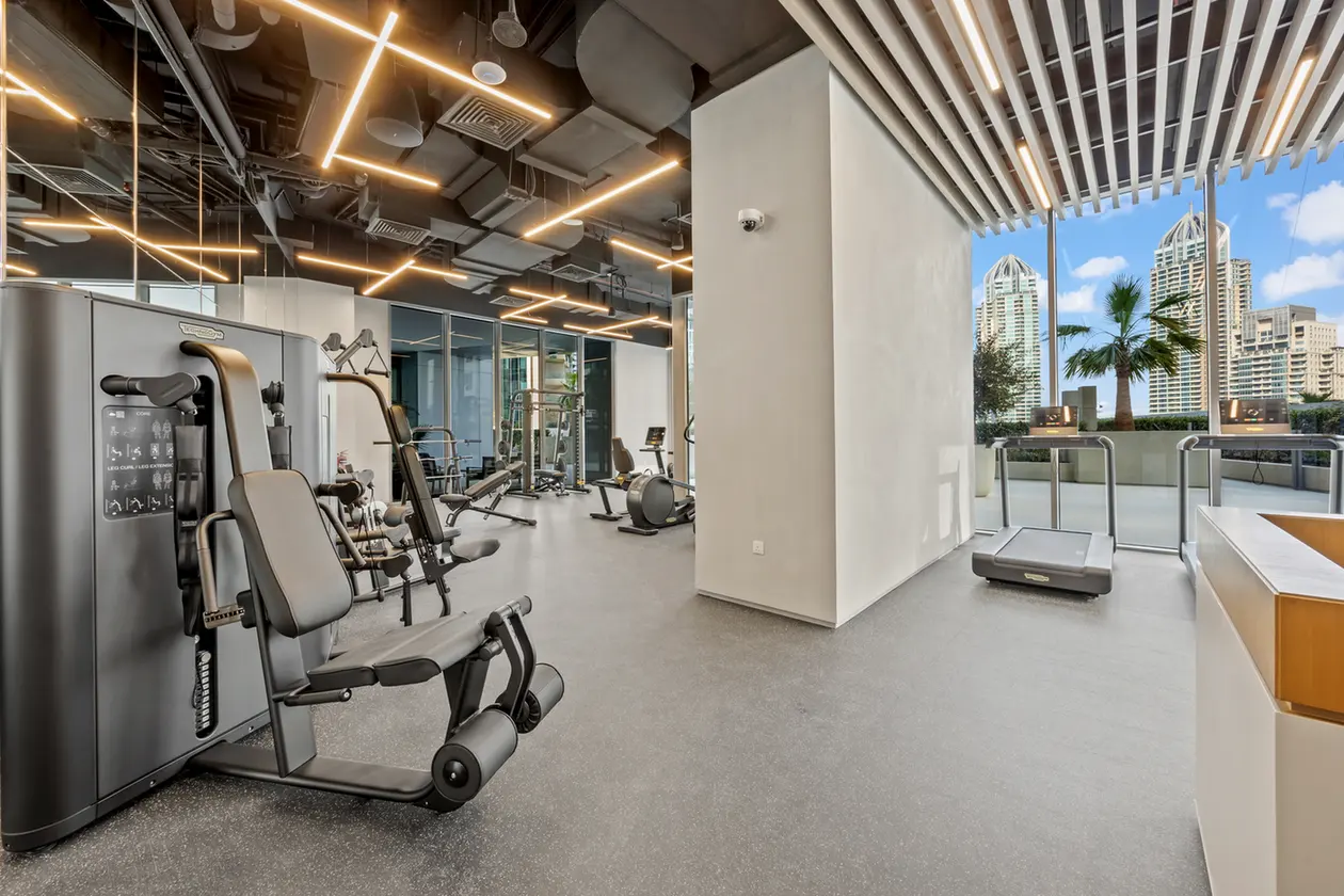Modern gym with weight machines near a large window offering city skyline views at the edge of the room.