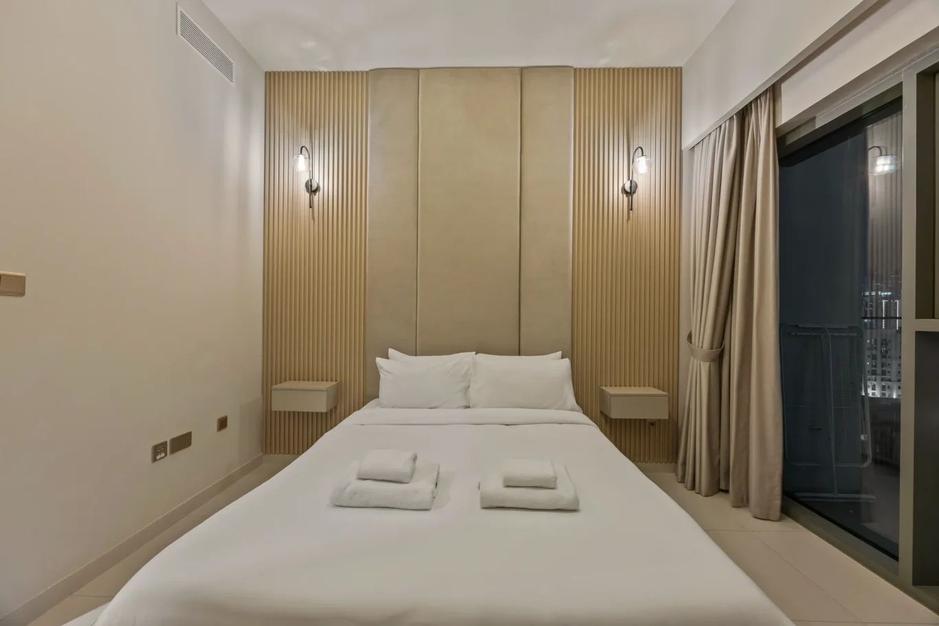 Modern hotel bedroom with a white bed, tall padded headboard, and vertical wood accent walls with bedside tables.
