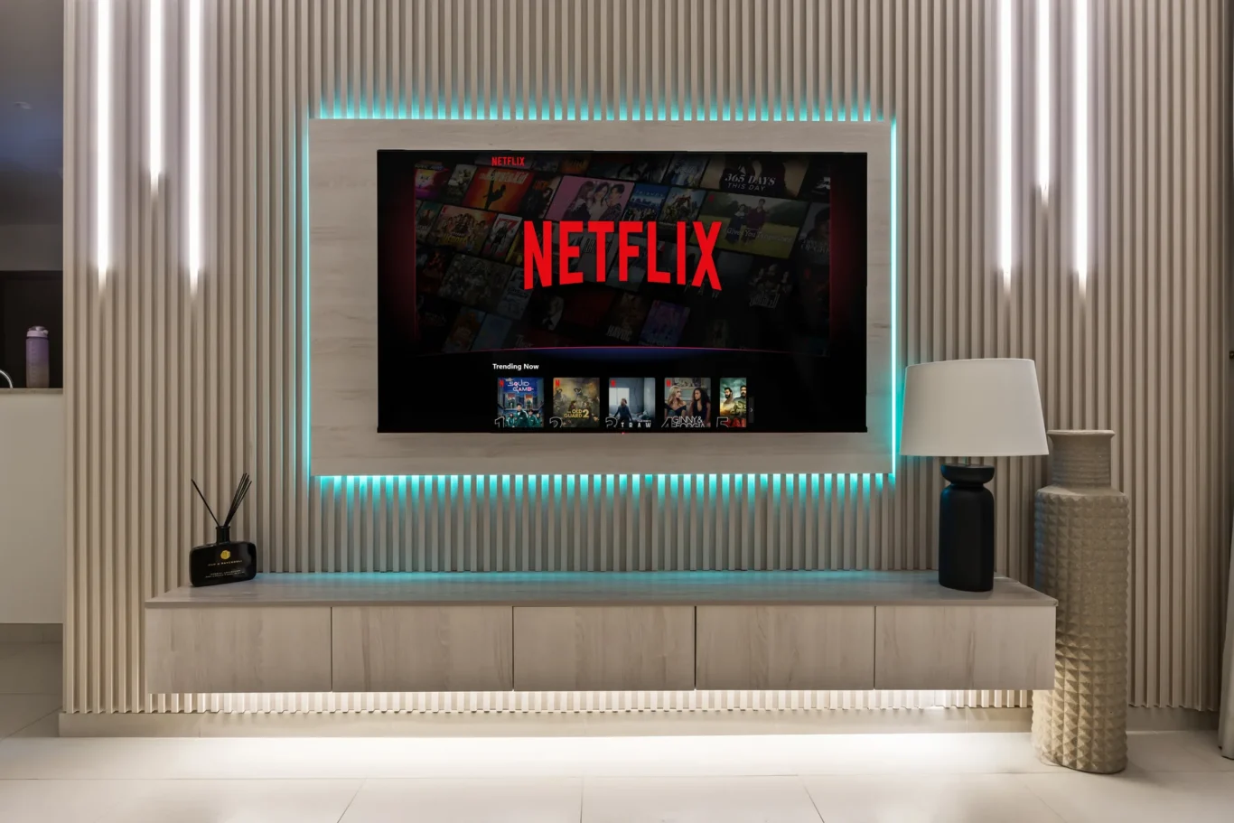 Wall-mounted TV displaying Netflix in a modern living room with teal backlighting and ribbed wall panels.