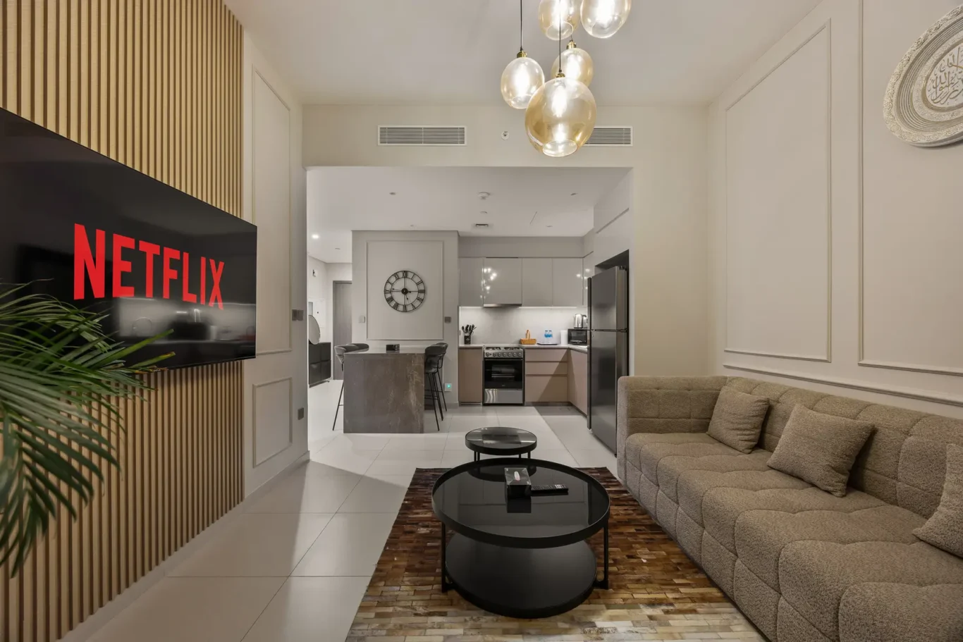 Living room with a large Netflix screen mounted on a wooden slat wall, beige sofa, and glass globe chandelier above a round coffee table frame.