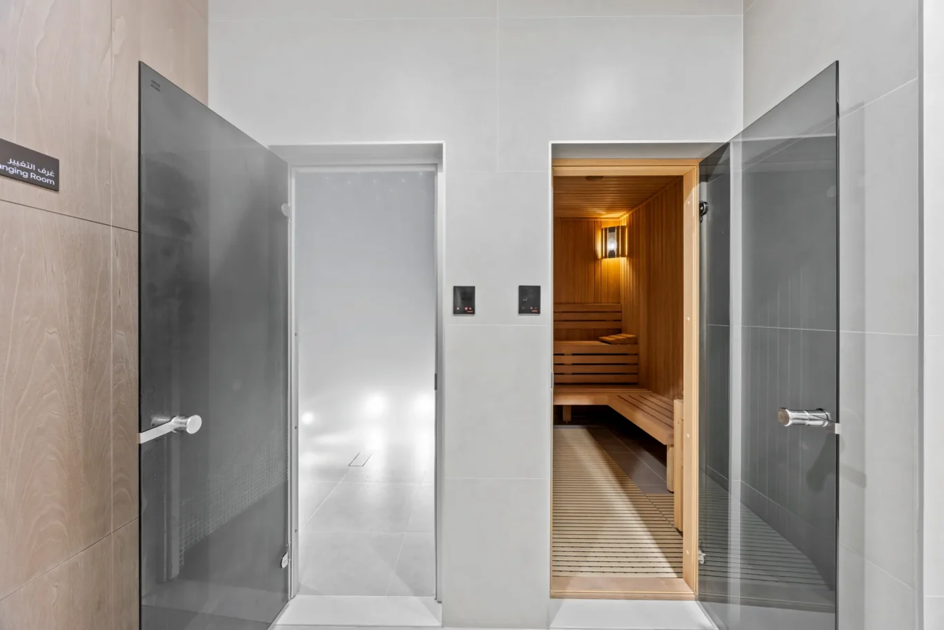 Entrance to a modern sauna area: glass doors with a wooden sauna interior and warm lighting visible inside.