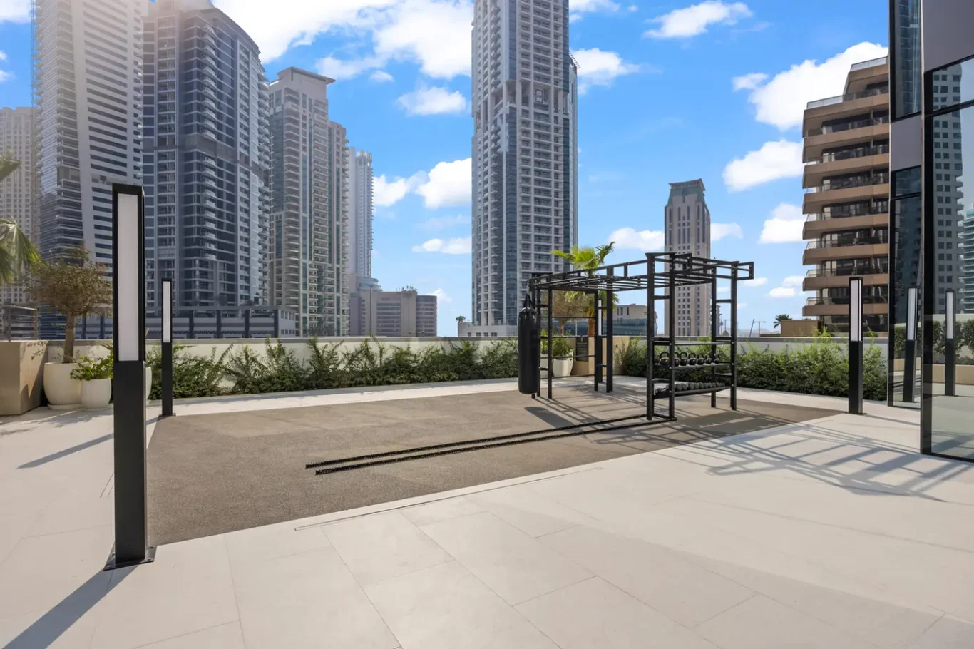 Rooftop outdoor gym with a metal workout frame and dumbbells, city skyline with tall buildings under a blue sky.
