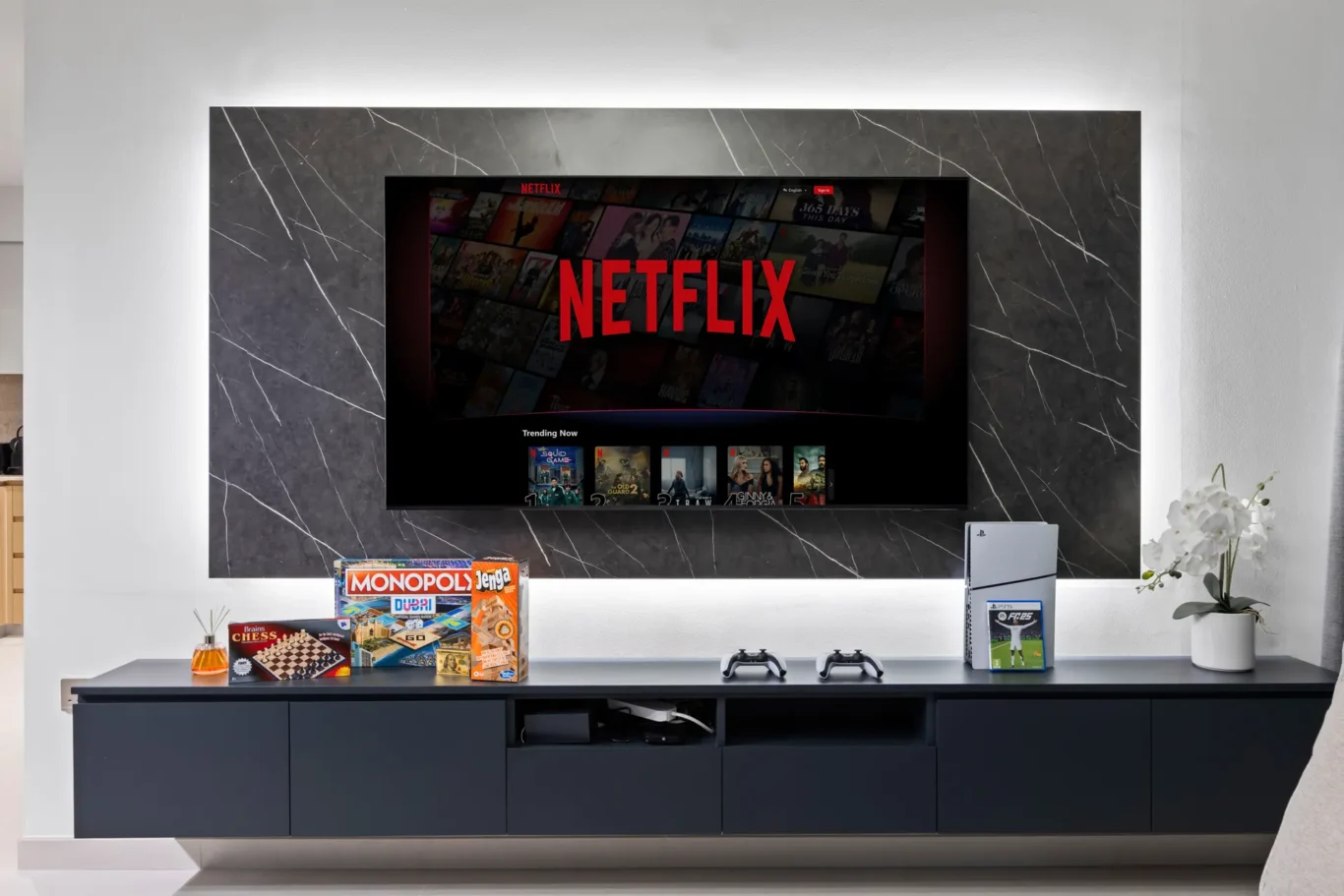 Flat-screen TV displaying Netflix logo mounted in a marble fireplace, with board games and a PlayStation below.
