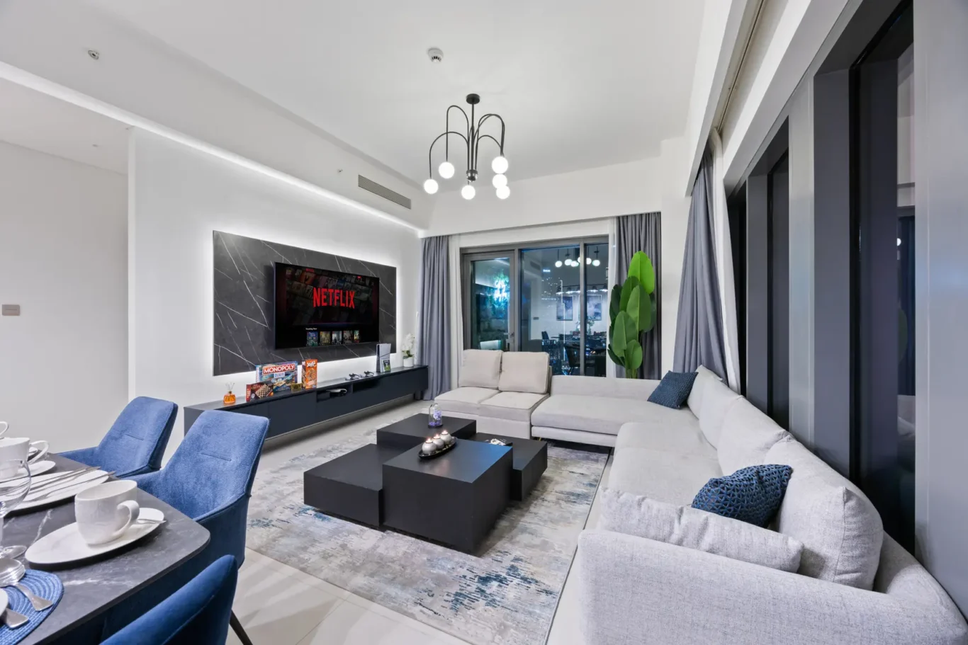 Modern living room with a wall-mounted Netflix TV, dark marble panel, and a large light-gray sectional sofa facing a low black coffee table.