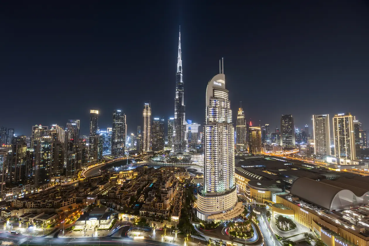 Nighttime aerial view of Dubai's skyline, centered on the Burj Khalifa with surrounding illuminated high-rises and roads.” (informative)