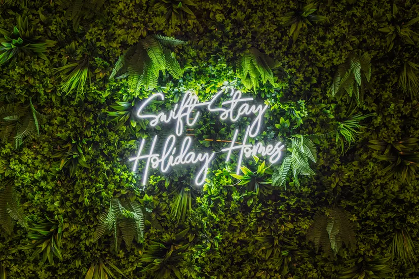 Neon script sign on a lush green living wall, advertising holiday homes as a backdrop.