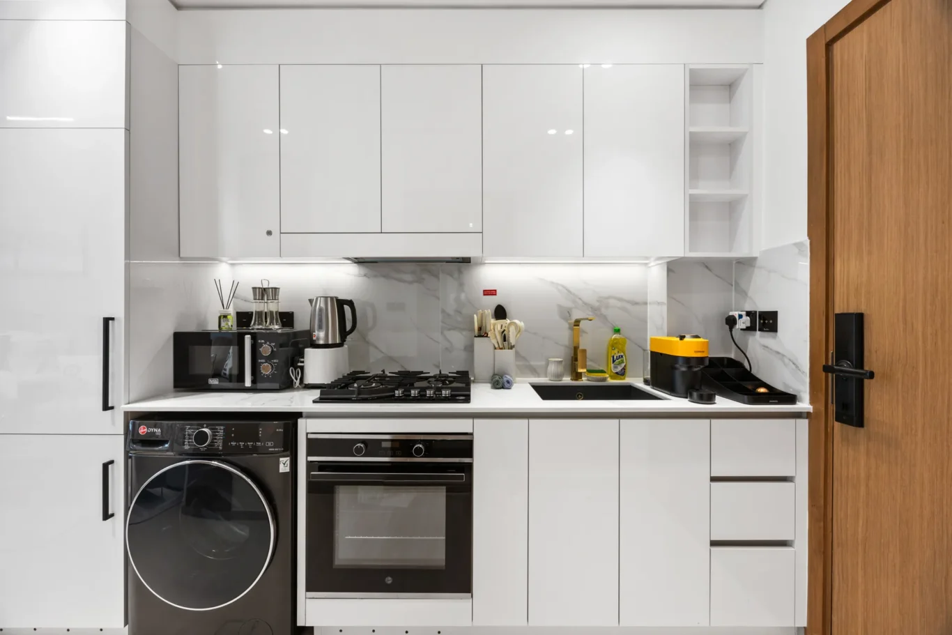 Modern white kitchen with glossy cabinets, marble backsplash, and integrated appliances (oven, hob, microwave).