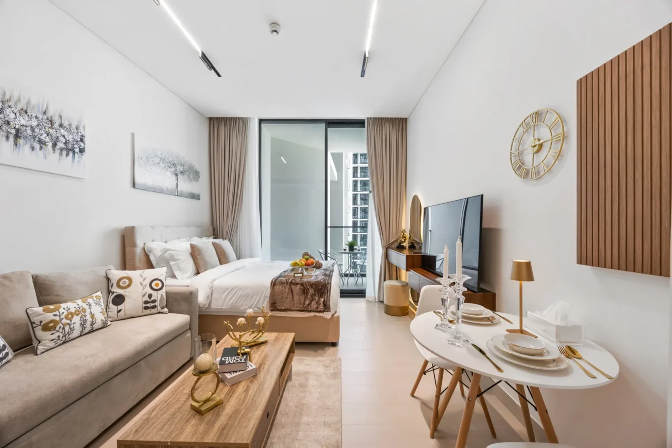 Open-plan living area with beige sofa, decorative pillows, and a wooden coffee table beside a balcony door with beige curtains.