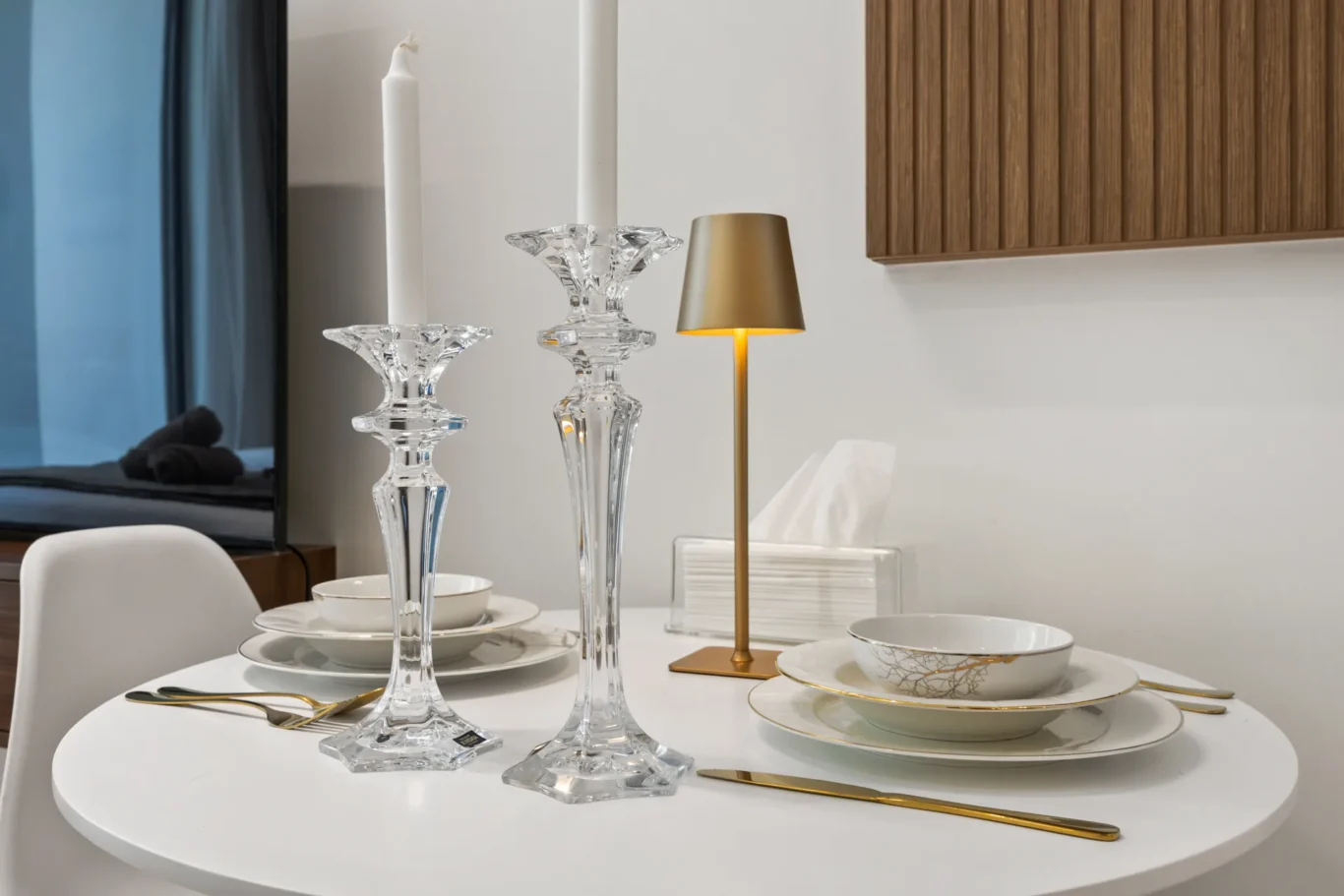 Table set for a formal meal with crystal candlesticks, gold-rimmed china, and a brass lamp.